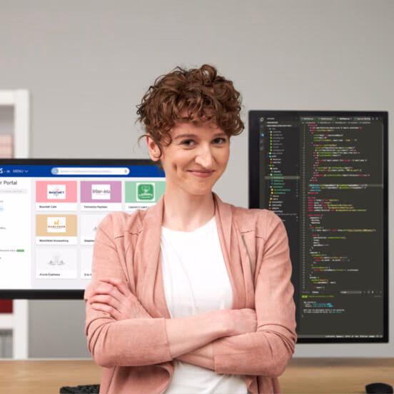 Coder standing with arms crossed at her desk with two monitors behind her. One with the Partner Portal interface, the other with PHP web code.