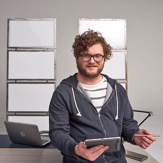 Web pro leaning on his desk with his arms crossed. There's a laptop in the background.