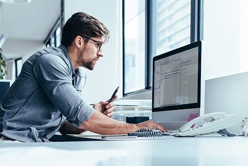 Man staring intently at a monitor with a pen in one hand