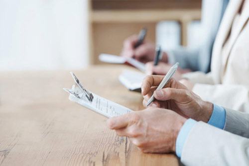 A pair of hands writing on a notepad on a clipboard