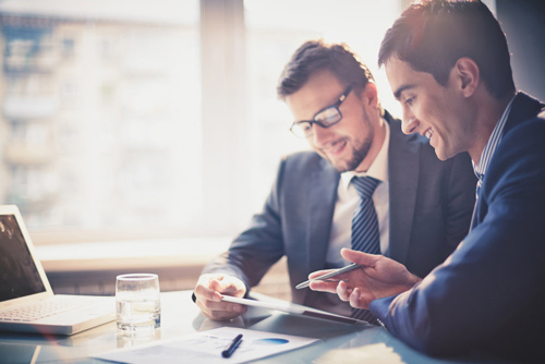 Two men in suits discussing something on a tablet